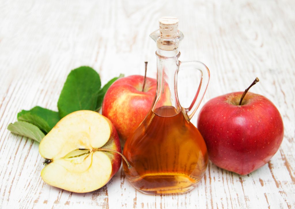 Äppelcidervinäger i fin flaska, färska äpplen vid sidan på ett träbord